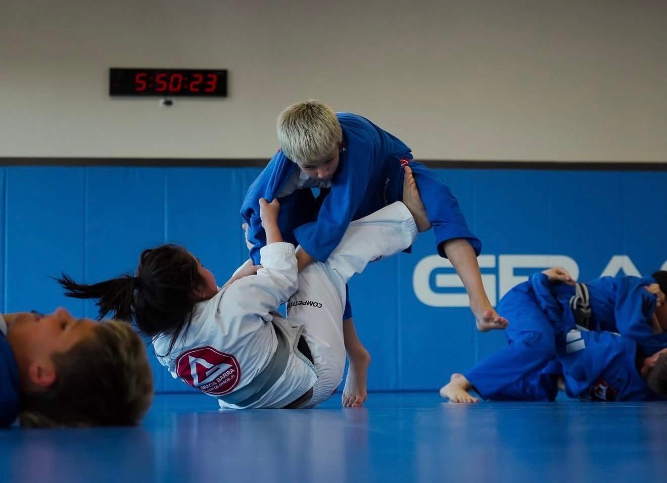 Two kids practice a guard position on the blue mats during a kids class