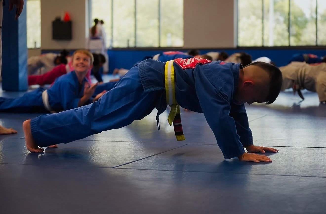 A boy with a yellow belt does a bear-crawl warm-up with his class