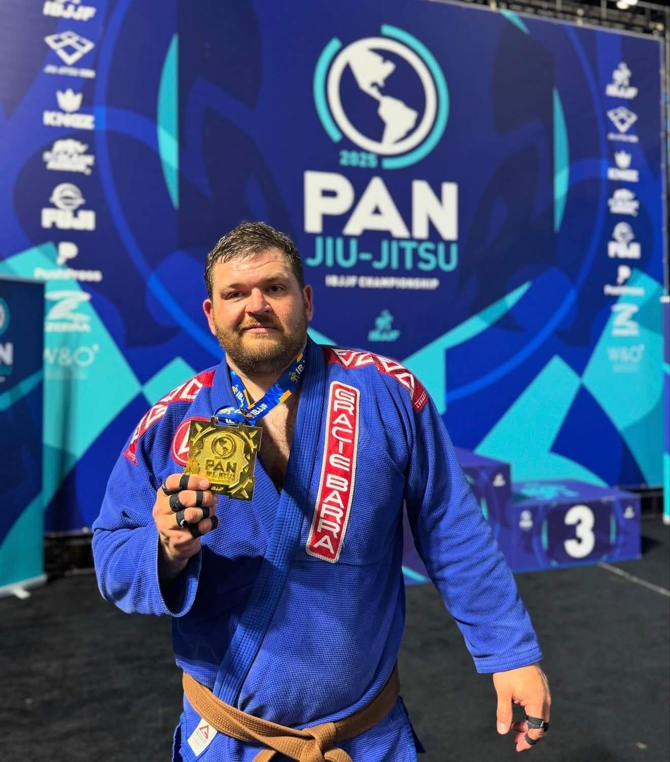 A brown belt in a Gracie Barra gi holds up a gold medal at the 2025 IBJJF Pan Jiu-Jitsu Championship